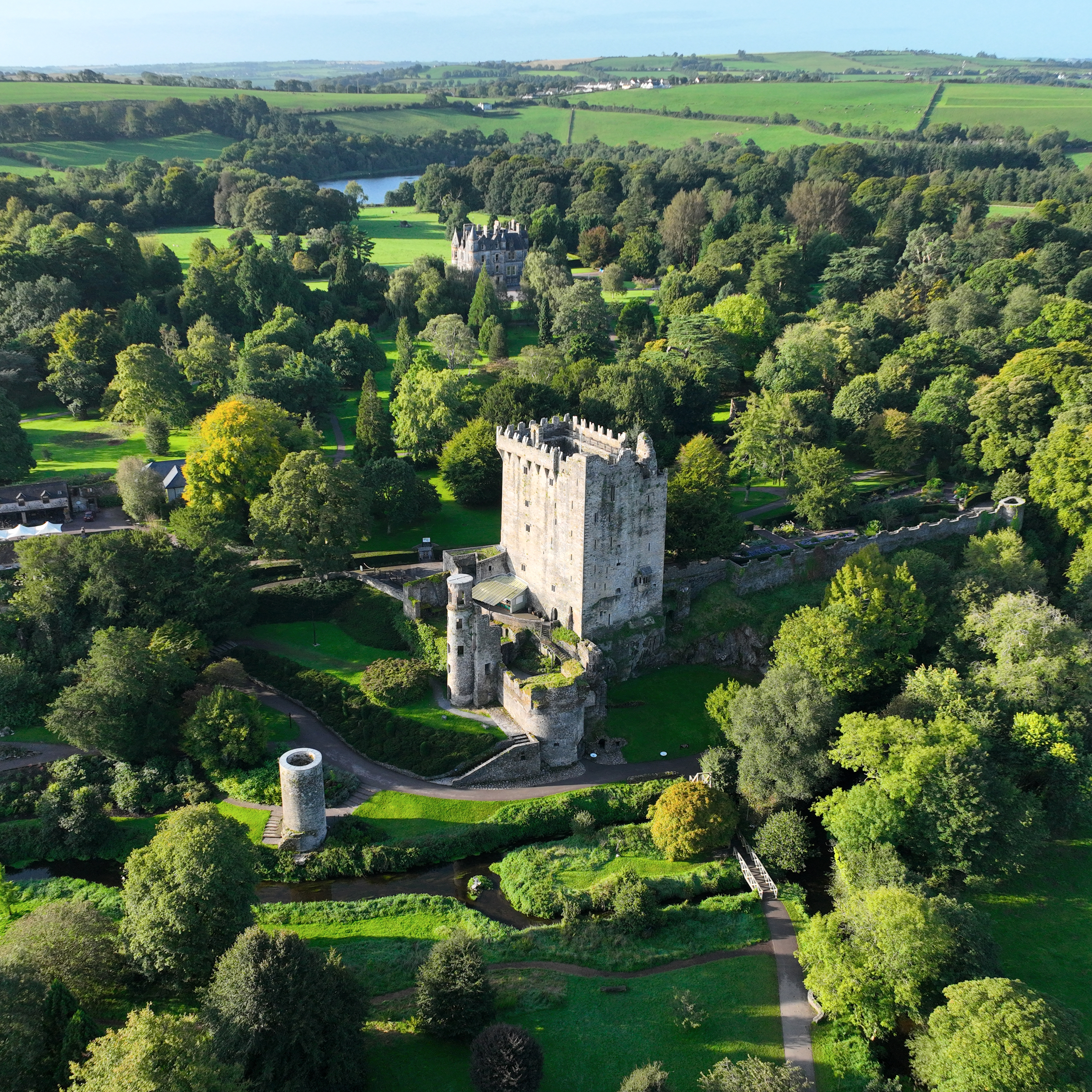 Aerial view of Blarney Castle surrounded by mature gardens, woodland and green countryside near Cork.
